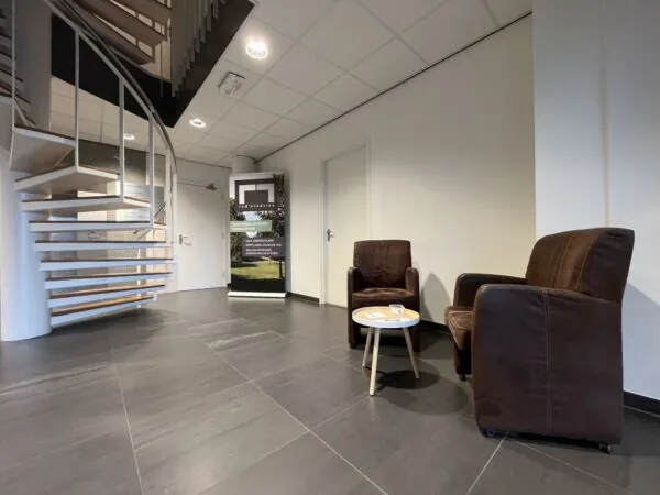 Wachtruimte met twee bruine fauteuils, een ronde tafel en een spiraaltrap in een kantoorpand in Leidse Rijn.